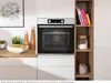 A modern kitchen scene featuring a built-in oven, a dish of food, decorative vases, and a bookshelf. Produktbild-Vorschau