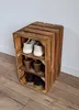 A wooden shoe rack made of crates with shoes and other items on its shelves, placed against a wall. Produktbild-Vorschau