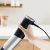 A hand holding the handle of an immersion blender in a kitchen setting. Produktbild-Vorschau