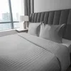 A neatly made bed with grey striped bedding and two pillows, set against a grey headboard. A window with a city view is visible in the background. Anteprima dell’immagine prodotto