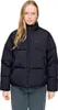 A woman wearing a black puffer jacket and grey pants, posing against a white background.
