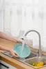 A person is washing a teal plate under a faucet with a water filter attached. Náhled obrázku produktu