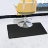 A black salon floor mat is placed on a light-colored floor in front of a salon chair. Some hair clippings are visible on the floor around the mat. Náhled obrázku produktu