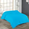 A bright turquoise duvet is laid out on a wooden floor in a bedroom setting. A large window with a grid pattern is visible in the background, along with a white nightstand and a table lamp. Produktbild-Vorschau