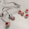 A pair of white in-ear headphones with red accents and several spare ear tips are laid out on a white surface. Produktbild-Vorschau