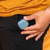 A hand is placing a blue earbud case into the pocket of black pants. Anteprima dell’immagine prodotto