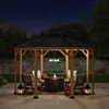 A wooden gazebo with a black roof is set up on a patio at night, featuring seating, a fire pit, and lanterns. Náhled obrázku produktu