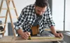 A man is using a tape measure to measure a piece of wood. Produktbild-Vorschau