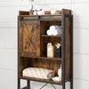 A close-up view of a wooden bathroom shelf unit with a sliding barn door, shelves holding towels, bottles, and a soap dish. Produktbild-Vorschau
