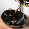 A black and gold marble-effect basin with a gold faucet, placed on a wooden surface. Náhľad obrázku produktu