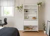 A white kitchen cabinet with glass doors and drawers, styled in a bedroom setting with plants and a bed. Anteprima dell’immagine prodotto