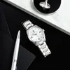 A watch and pen are placed on a black surface, with a spinning top in the background. Náhľad obrázku produktu