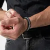 A man's wrist wearing a bracelet, with his other hand adjusting it. Anteprima dell’immagine prodotto