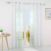 A white sheer curtain hangs in front of a window with a view of a lake and trees. A small wooden table with a vase of flowers and a teacup is to the left. Produktbild-Vorschau