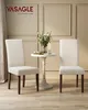 Two cream-colored dining chairs flank a small, ornate white table with a floral arrangement and candles. Produktbild-Vorschau