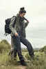 A woman wearing a backpack and outdoor clothing poses in a grassy, outdoor setting. Náhled obrázku produktu
