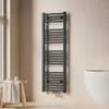 A dark grey towel radiator is mounted on a light beige wall next to a white bathtub. A wooden stool with a folded towel and some small containers is placed to the left of the radiator. Produktbild-Vorschau