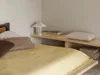 A bed with pillows and a blanket, a bedside table with a lamp and books. Produktbild-Vorschau