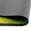 A close-up view of the edge of a rug or mat, showing the texture of the green fibers and the gray backing. Voir les images du produit