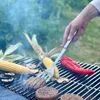 A hand is using tongs to flip burgers on a grill with corn and peppers. Anteprima dell’immagine prodotto