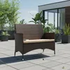 A brown rattan bench with a beige cushion sits on a tiled patio, surrounded by potted plants and a modern building. Anteprima dell’immagine prodotto