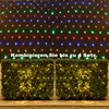 A net light string with colorful LEDs is displayed against a dark background, with two bushes decorated with yellow lights in the foreground. Voir les images du produit