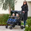 A woman is pushing a double stroller with two babies in it outdoors. Produktbild-Vorschau