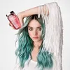 A woman with teal hair holds a pink bottle of Kérastase shampoo, posing with her arm raised. Anteprima dell’immagine prodotto