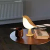 A bird-shaped lamp sits on a wooden table next to a cup and books. Anteprima dell’immagine prodotto