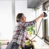 A woman is cleaning a window with a handheld steam cleaner. Produktbild-Vorschau
