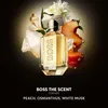 A bottle of BOSS The Scent for Her perfume is surrounded by elements representing its fragrance notes, including peach slices, white flowers, and crystals, against a dark, gradient background. Anteprima dell’immagine prodotto