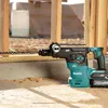 A cordless hammer drill with a drill bit attached is shown on a construction site. Podgląd zdjęcia produktu