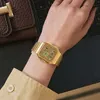 A person wearing a gold watch on their wrist, with a brown wallet and a laptop in the background. Voir les images du produit