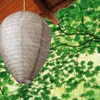 A wasp nest decoy hanging from a wooden overhang, with green foliage in the background. Produktbild-Vorschau