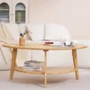 A light wood oval coffee table with a lower shelf, placed in front of a white sofa. Voir les images du produit