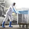 A worker in a food processing plant is pushing a large stainless steel container on wheels. Produktbild-Vorschau
