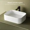 A white ceramic vessel sink filled with water, with a black faucet behind it, placed on a textured olive green vanity. Produktbild-Vorschau
