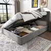 A grey upholstered bed with its storage compartment open, revealing stored items. Podgląd zdjęcia produktu