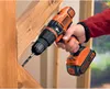 A person is using a Black & Decker cordless drill to drill into a wooden beam. Produktbild-Vorschau