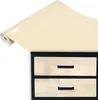 A roll of cream-colored glossy vinyl wrap is unfurled over a black-framed set of two cream-colored drawers with black handles. Produktbild-Vorschau