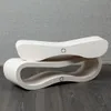 Two white, curved cat scratching posts are stacked on top of each other, with a grey textured wall in the background and a dark wooden floor in the foreground. Produktbild-Vorschau