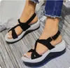 Schwarz-weiße Keilsandalen mit überkreuzten Riemen an den Füßen einer Person, mit blauer Jeans Anteprima dell’immagine prodotto