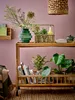 A wooden bar cart styled with decorative items including a vase of flowers, books, and plants against a pink wall. Produktbild-Vorschau