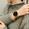 A person wearing a grey sweater and a gold smartwatch. Produktbild-Vorschau