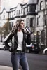 A woman is standing on a city street, holding and drinking from a black thermos. Anteprima dell’immagine prodotto