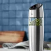 A close-up shot of a WMF electric mill filled with green peppercorns, set against a blurred background of blue tiles and a wooden cutting board. Anteprima dell’immagine prodotto
