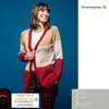 A woman wearing a cardigan and plaid pants, posing against a blue background. Produktbild-Vorschau