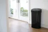A black sensor trash can is placed next to a white wall and a glass door. Náhľad obrázku produktu