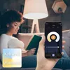 A woman is reading a book on a couch while holding a smartphone that displays a smart lamp control app. Produktbild-Vorschau