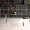 A khaki steel garden table with a chair in a modern kitchen setting with black tiled walls. Produktbild-Vorschau